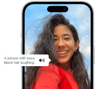 iPhone 15 engedélyezett hangalámondással, amely egy mosolygó, hullámos fekete hajú személy képét írja le.